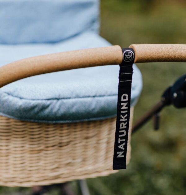 NATURKIND Kinderwagen Ida - erhältlich bei Hautnah Naturwaren Eine Nahaufnahme von einem braunen Griff eines Kinderwagens. In der Mitte ist ein Anhänger mit der Aufschrift "NATURKIND".